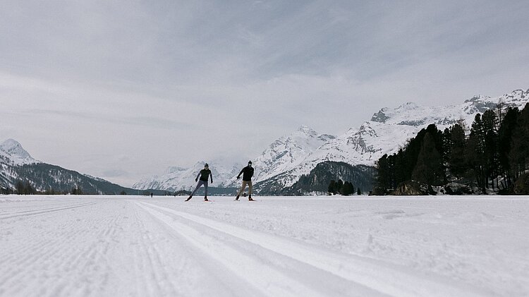 Zwei Langläufer auf einer verschneiten Loipe am Silsersee im Schweizer Engadin, im Hintergrund