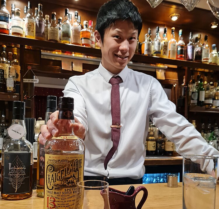 Barkeeper hinter einer Theke mit Whiskyflaschen serviert einen Single Malt in einem schottischen Pub